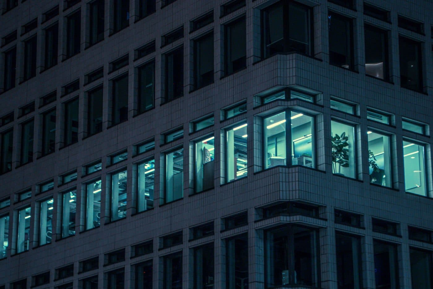 A single lit office window in an otherwise dark building at night