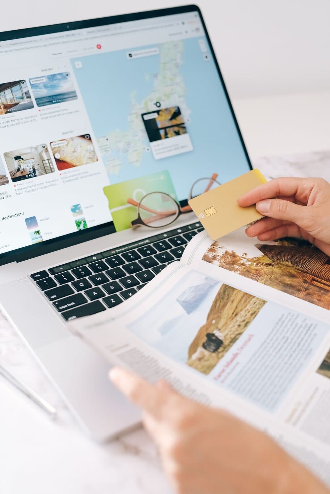 A hand holding a bank card over a laptop showing a travel booking