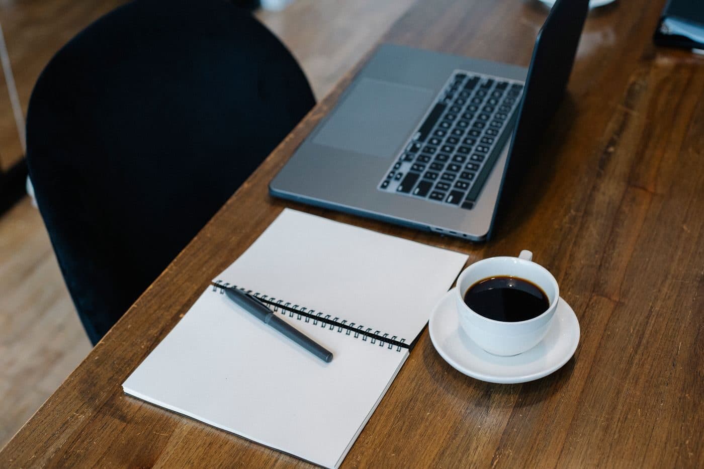 A laptop and notepad beside a cup of coffee on a desk