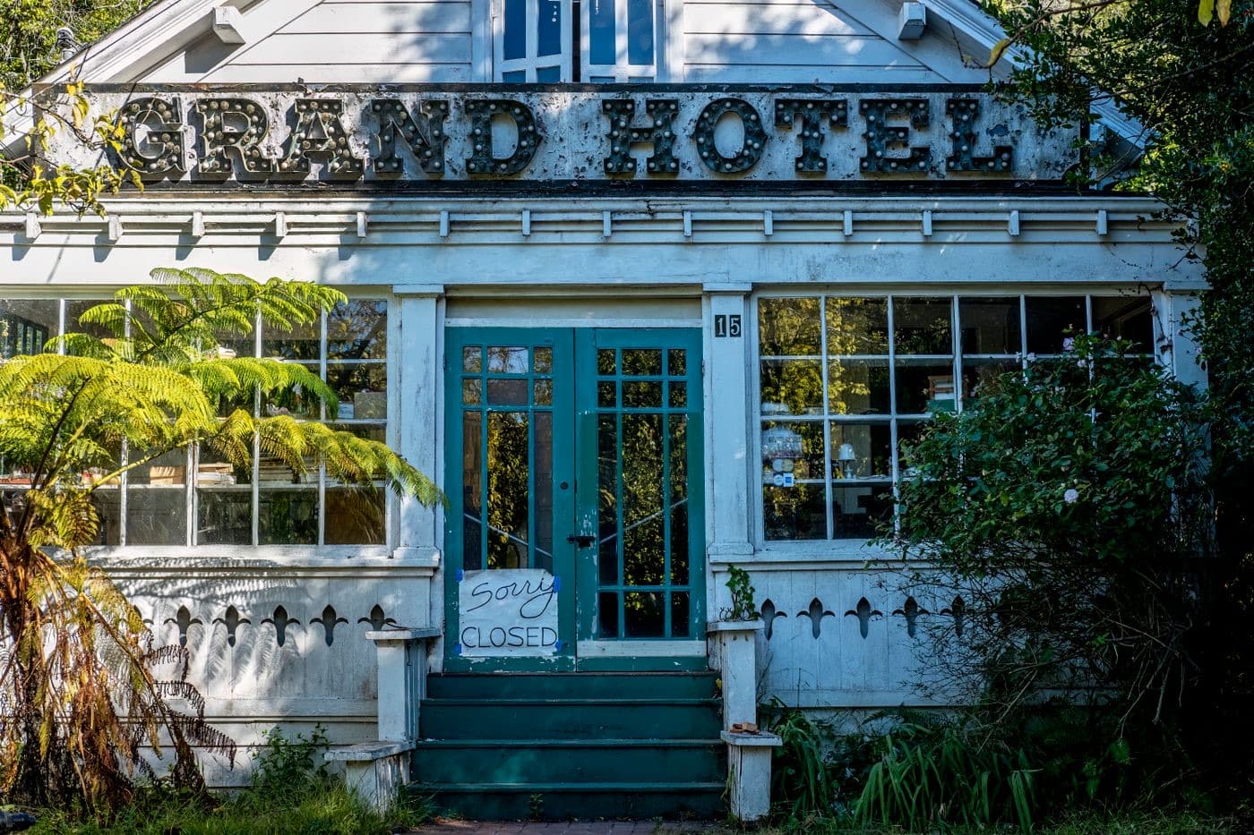 An abandoned hotel with a closed sign in an overgrown garden