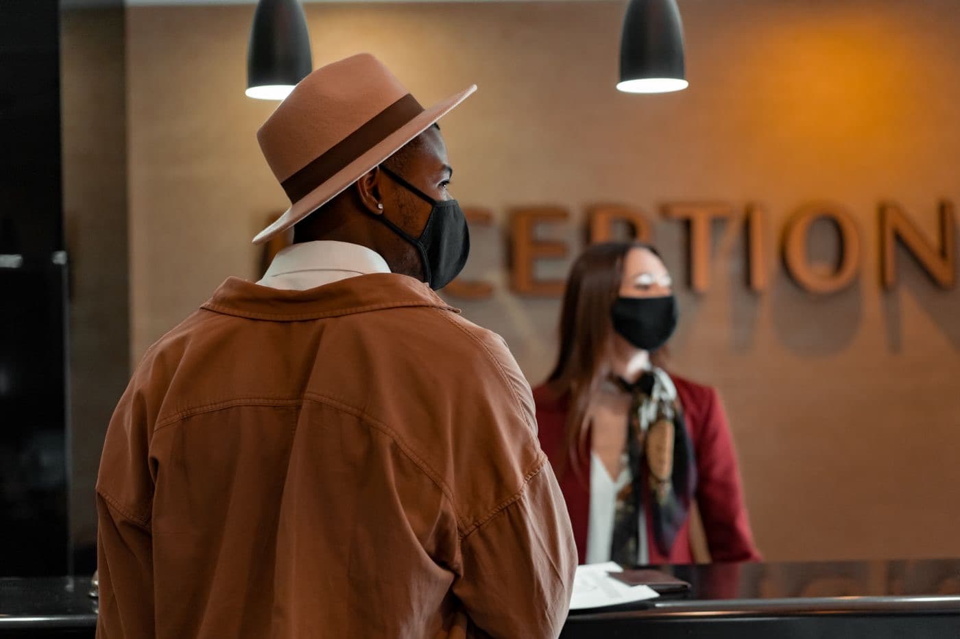 A guest and a masked receptionist at a hotel front desk