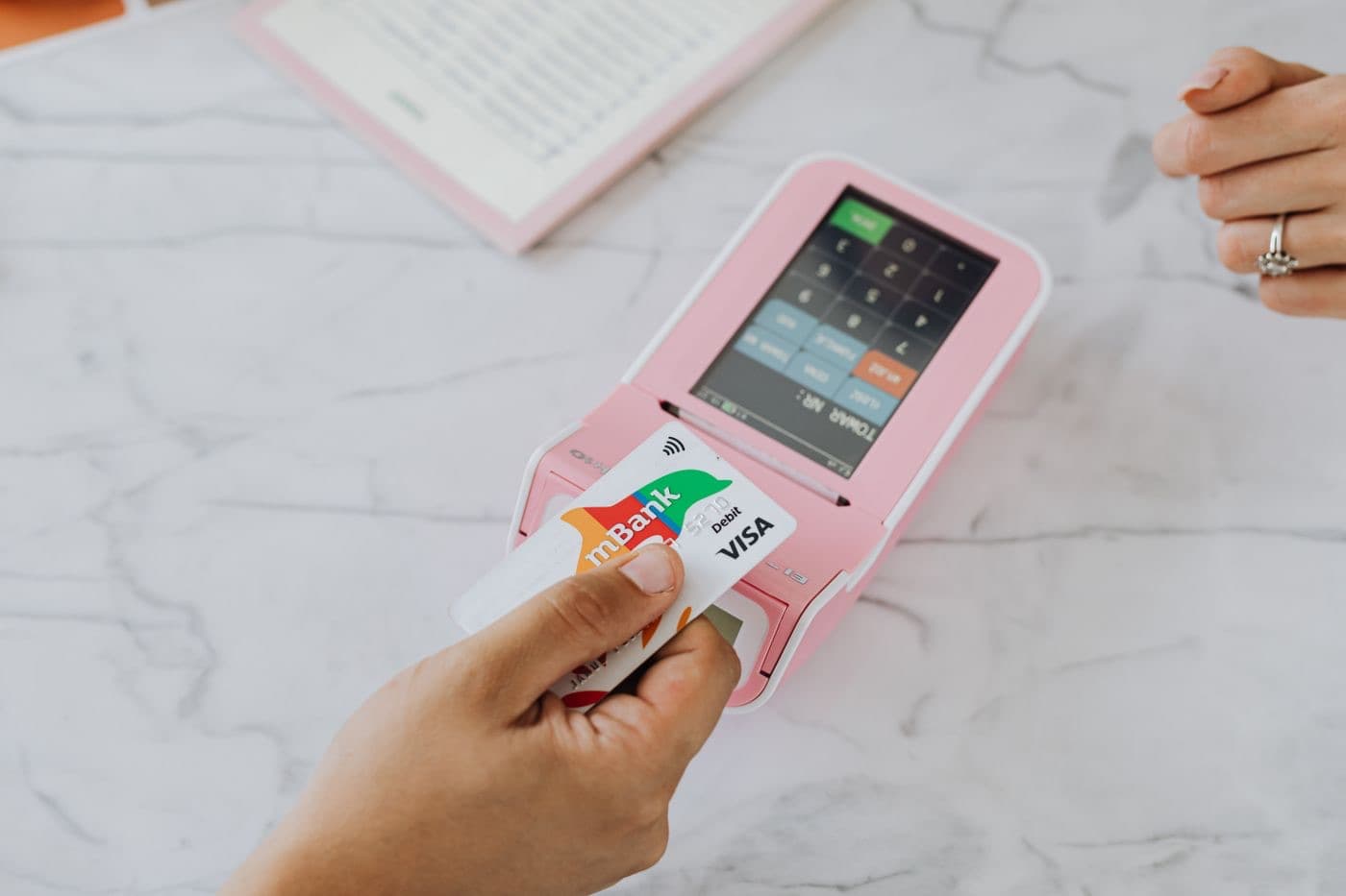 A hand tapping a contactless card on a payment terminal