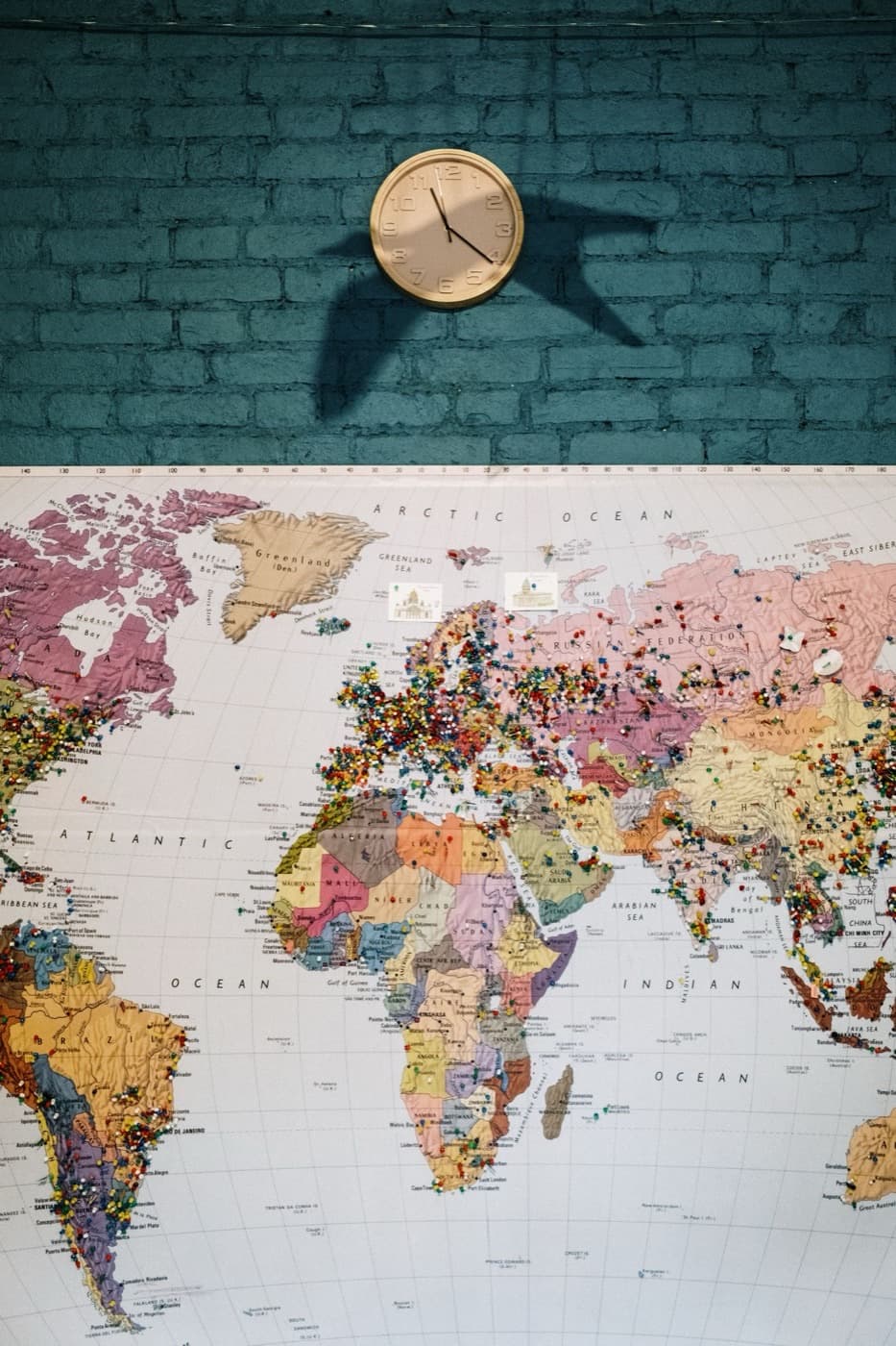 A vintage wall clock above a world map with colourful pins